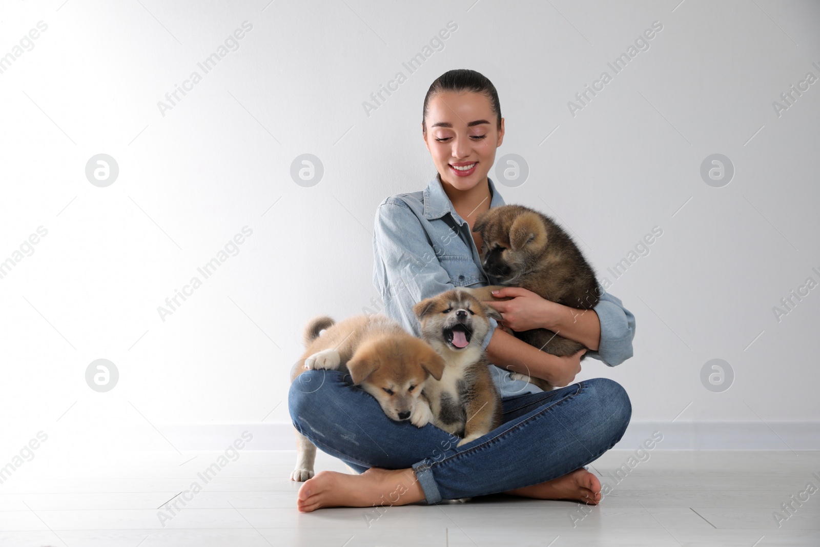 Photo of Woman with Akita Inu puppies sitting on floor near light wall