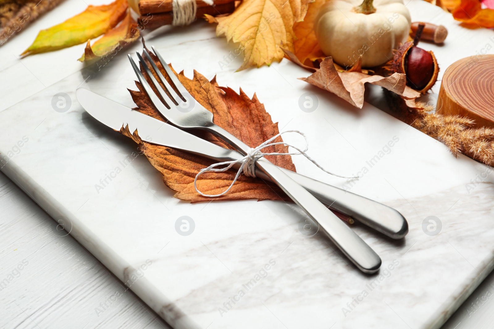 Photo of Cutlery with dry leaf on marble board, closeup. Table setting elements