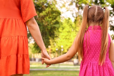 Photo of Little girl and her mother holding hands outdoors. Family weekend