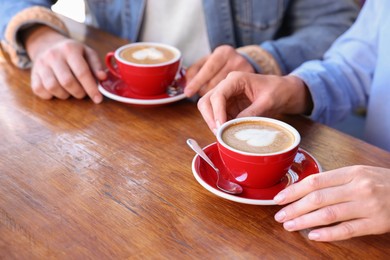 Couple with cups of aromatic coffee at wooden table, closeup