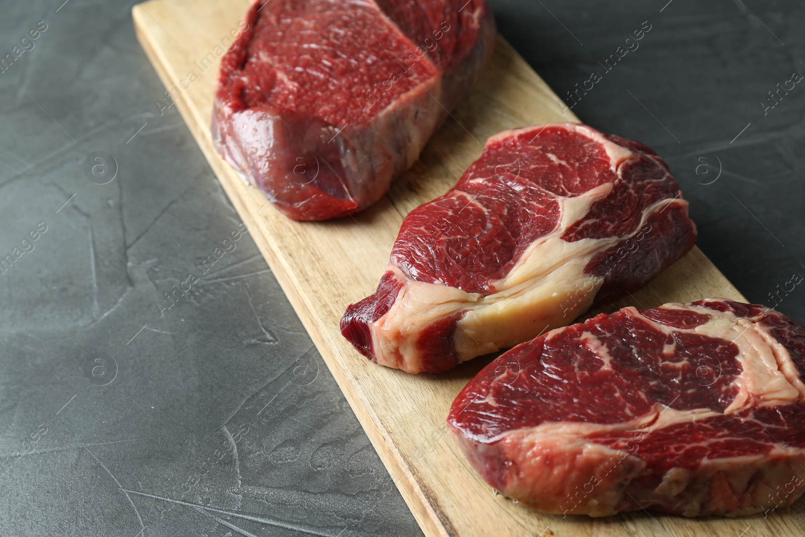 Photo of Wooden board with pieces of raw beef meat on grey table