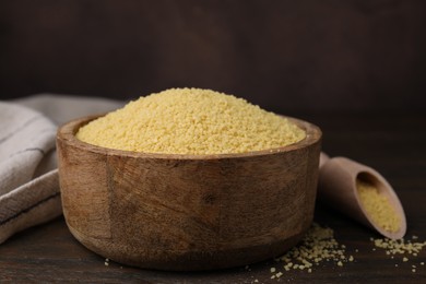 Photo of Raw couscous in bowl on wooden table, closeup