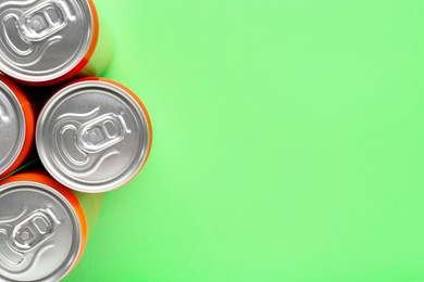 Energy drink in cans on light green background, top view. Space for text