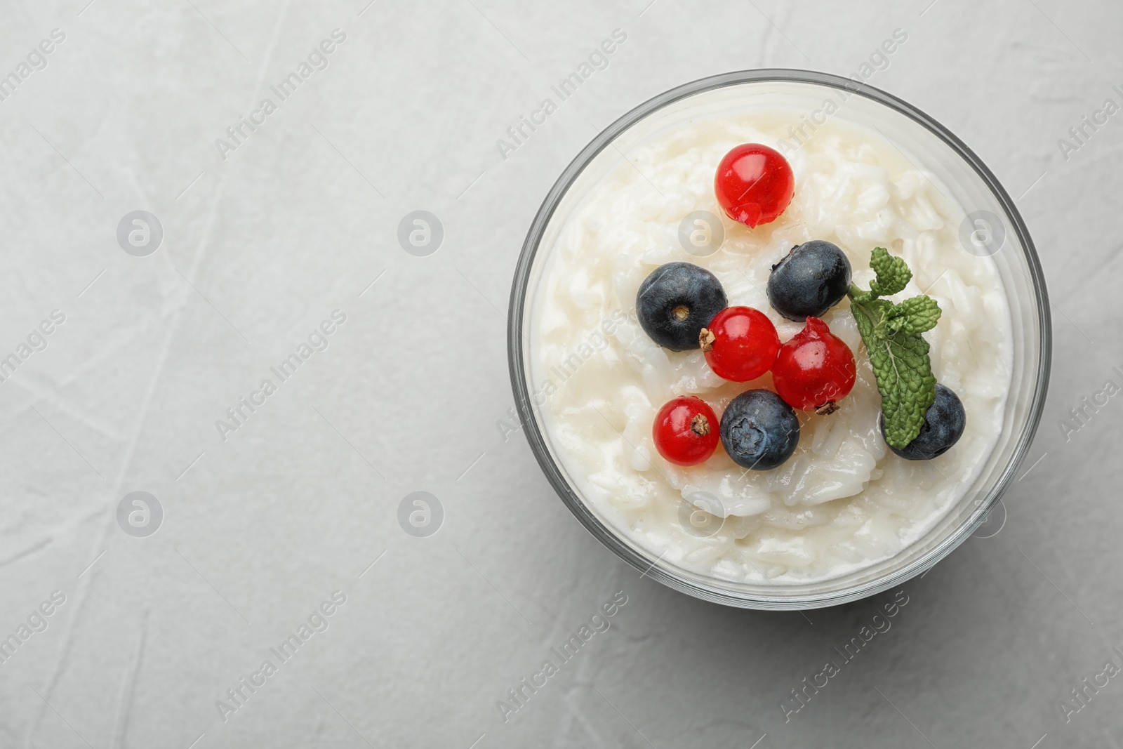 Photo of Delicious rice pudding with berries on light table, top view. Space for text