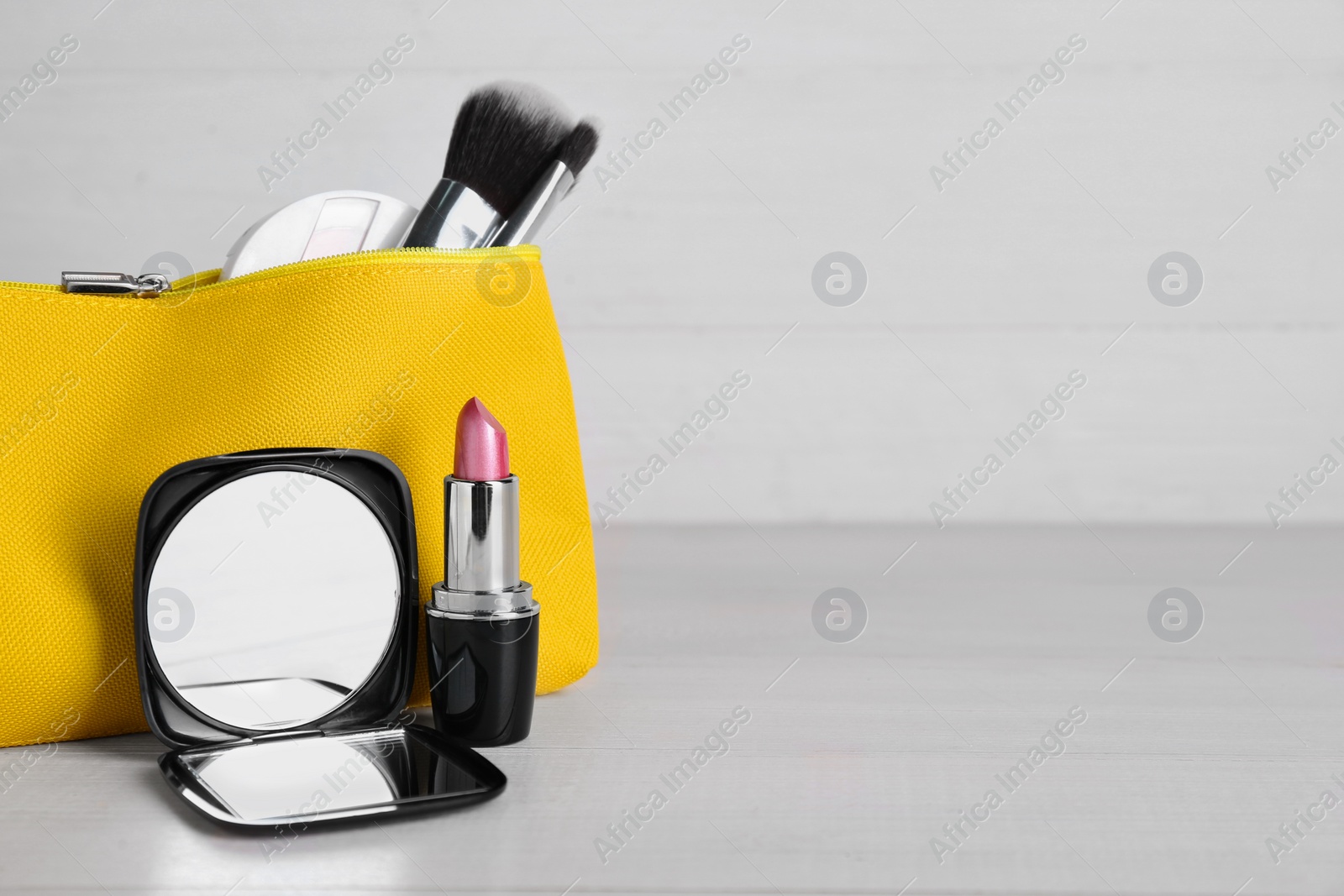 Photo of Stylish pocket mirror, lipstick and cosmetic bag with makeup products on white wooden table, space for text