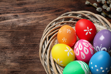 Photo of Colorful Easter eggs in decorative nest on wooden background, closeup. Space for text
