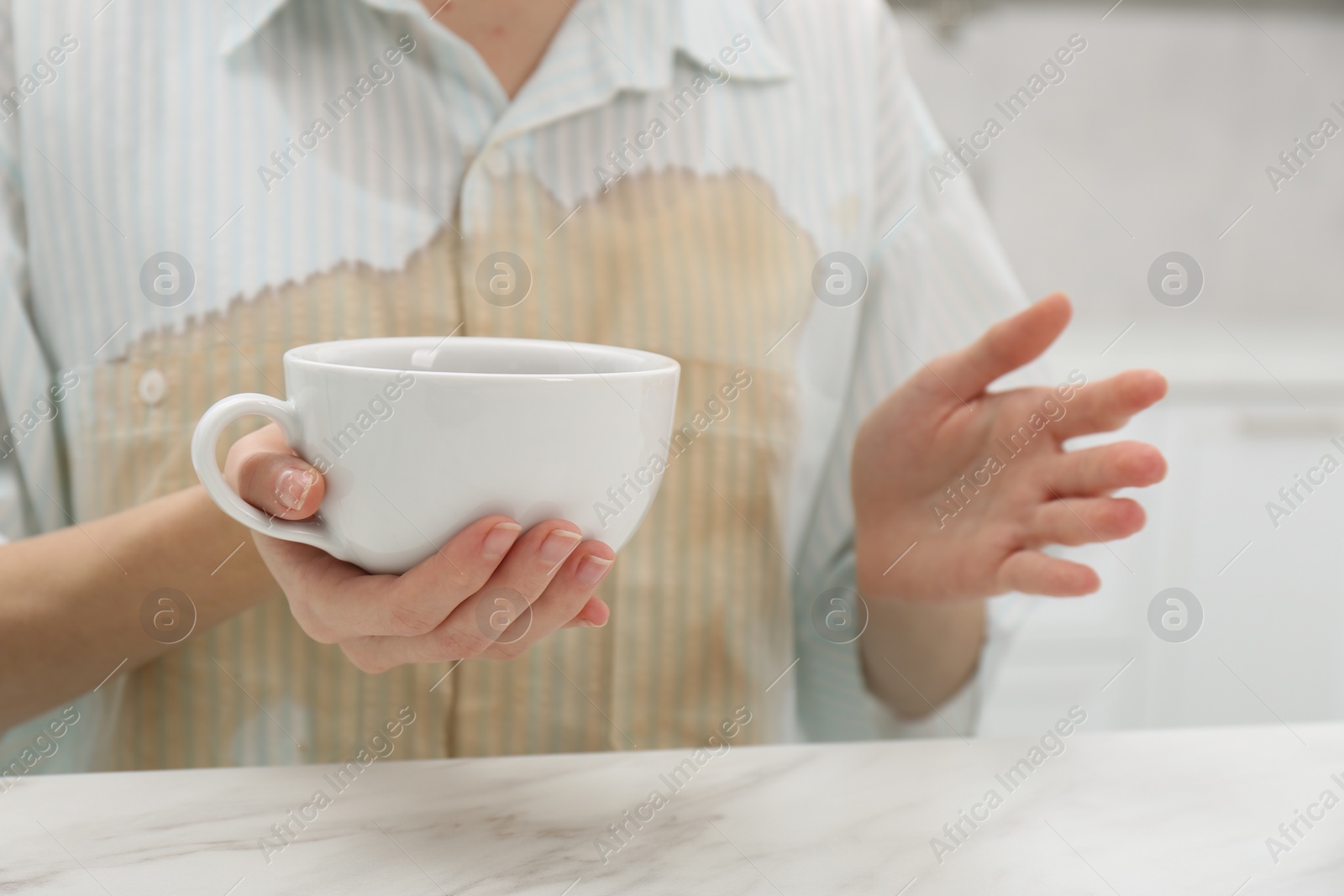 Photo of Woman with spilled coffee over her shirt sitting at marble table indoors, closeup