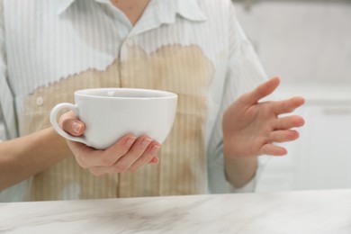 Woman with spilled coffee over her shirt sitting at marble table indoors, closeup