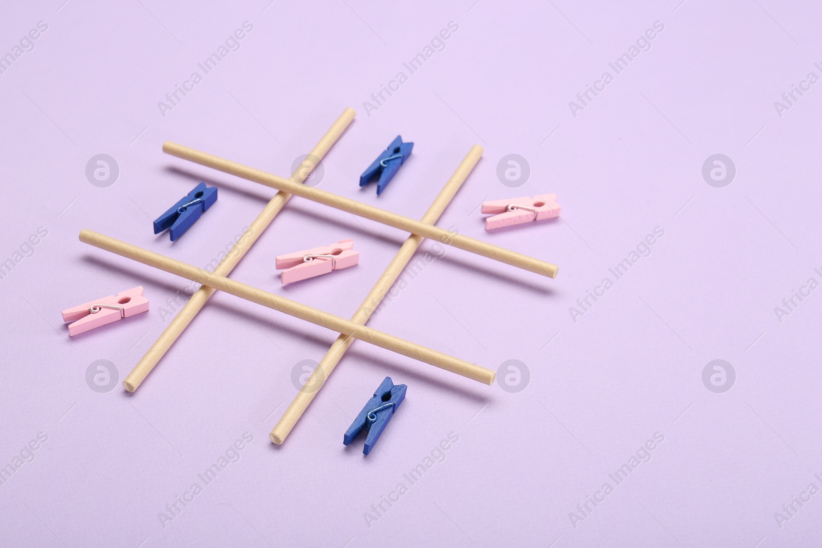 Photo of Tic tac toe game made with clothespins on lilac background