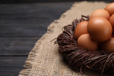Photo of Fresh chicken eggs in nest on black wooden table, closeup. Space for text