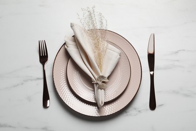 Photo of Plates with fabric napkin, decorative ring and cutlery on white marble table, flat lay