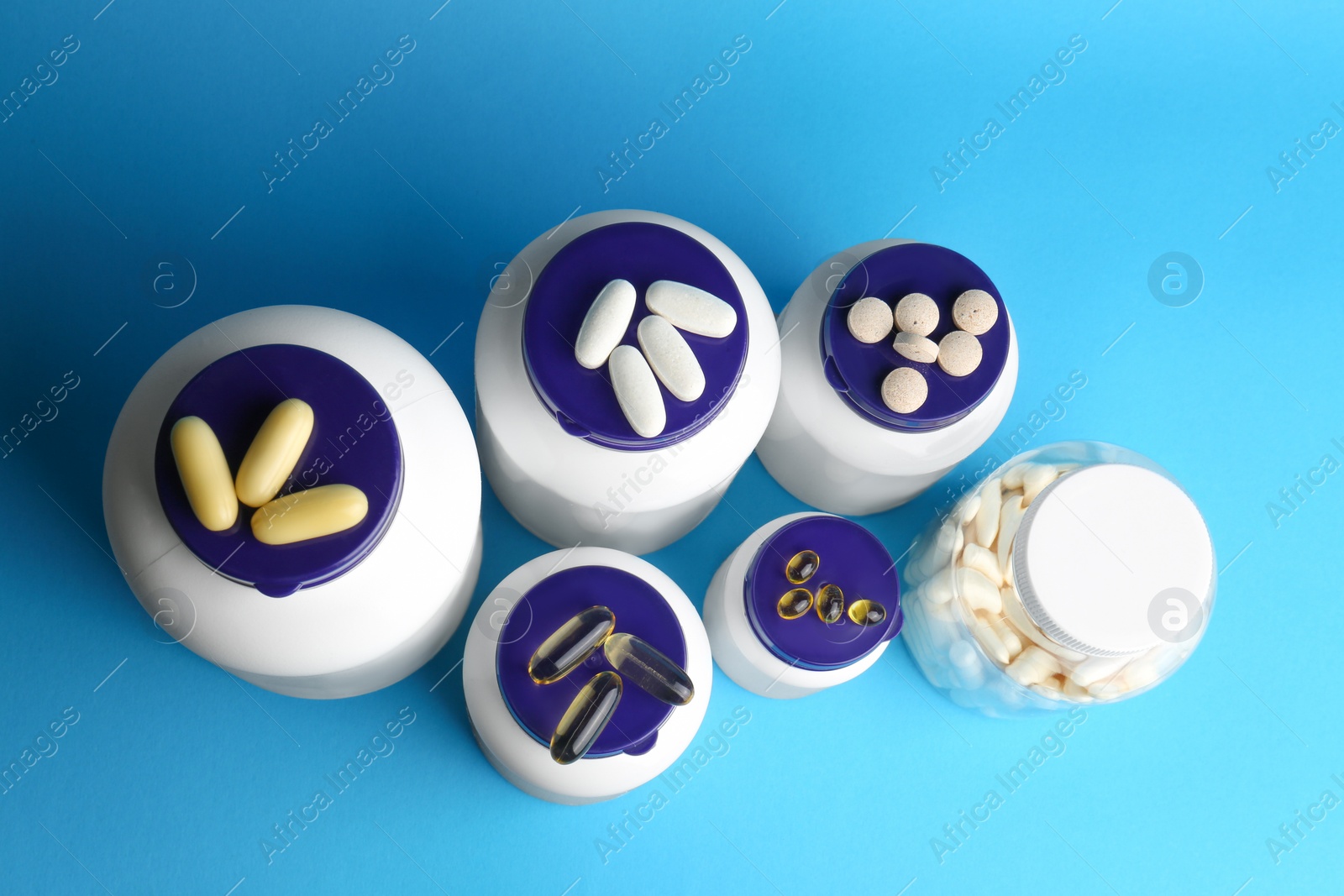 Photo of White medical bottles and different pills on light blue background, flat lay