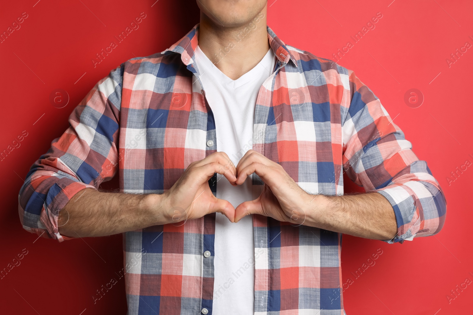 Photo of Man making heart with hands on red background, closeup