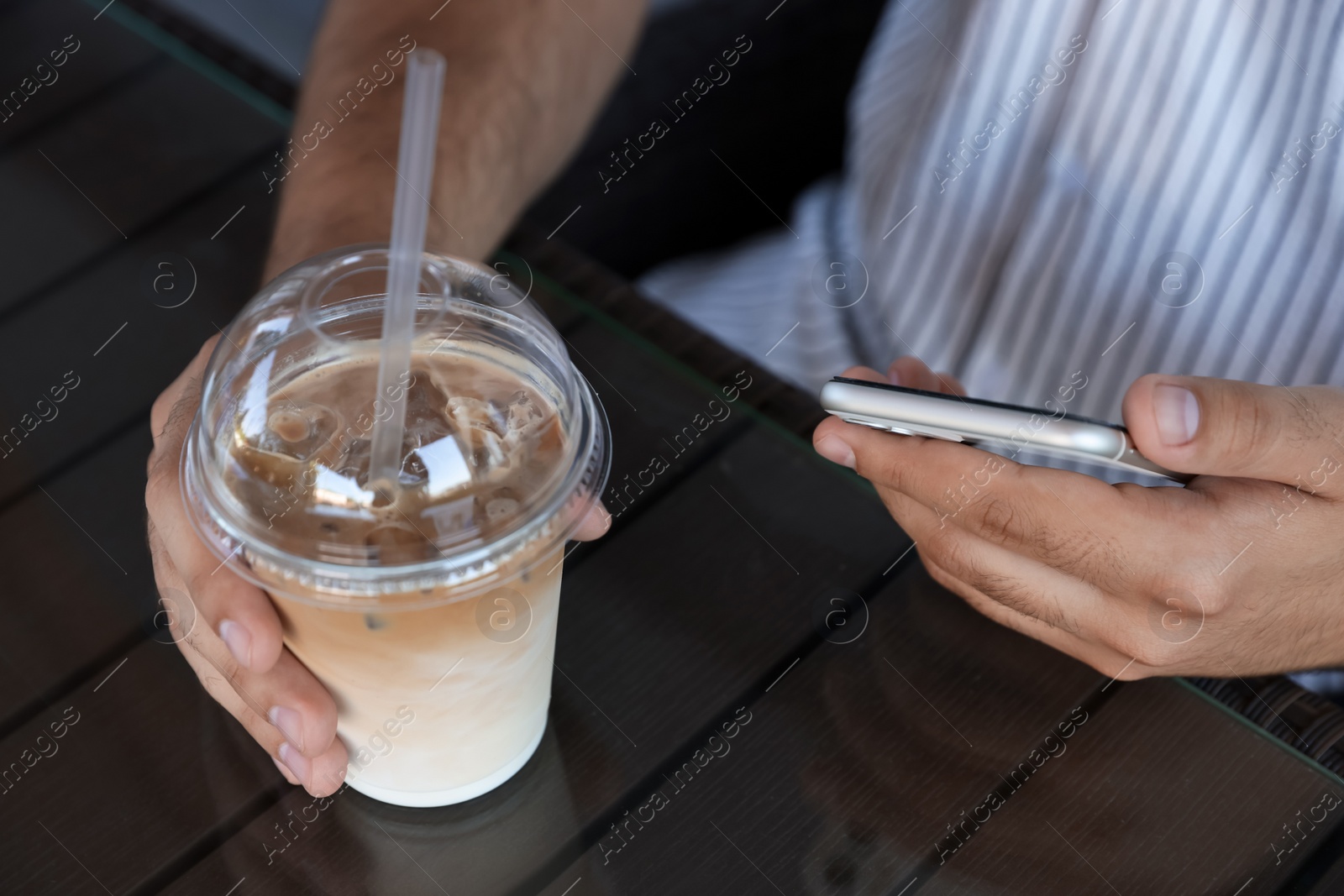 Photo of Man with smartphone and plastic takeaway cup of delicious iced coffee at table in cafe, closeup