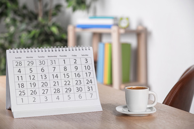 Calendar and cup of coffee on wooden table against blurred background