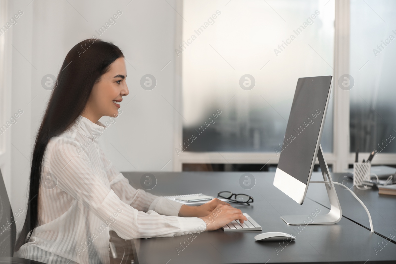 Photo of Happy woman using modern computer at black desk in office
