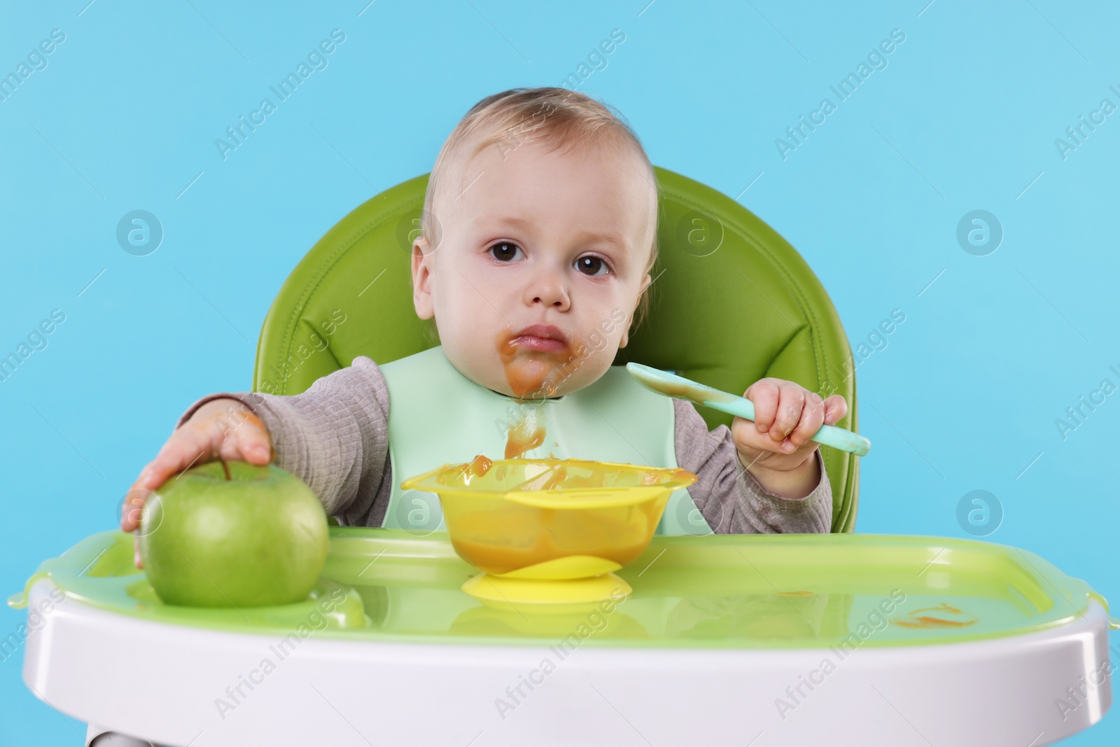 Photo of Cute little baby eating healthy food in high chair on light blue background