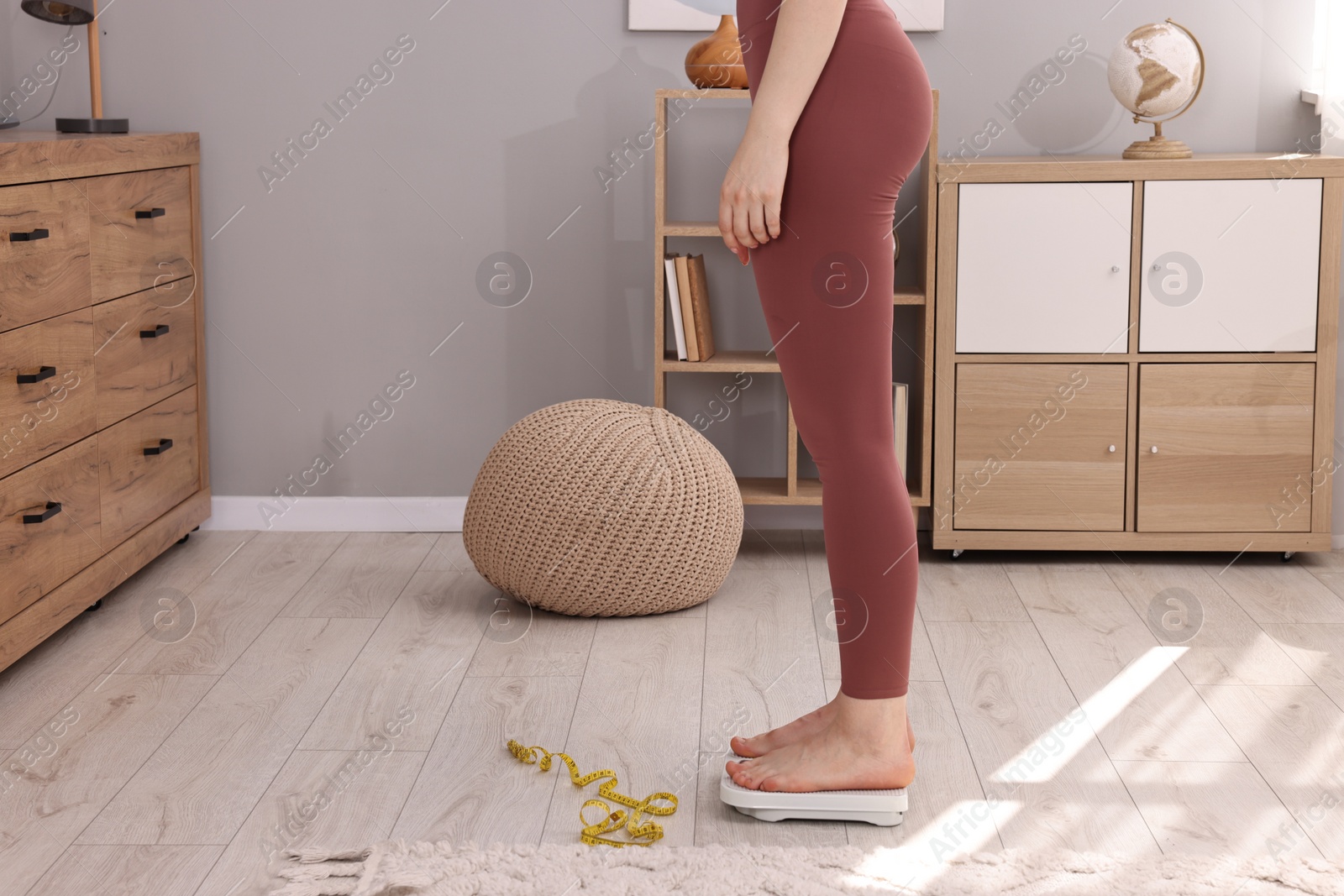 Photo of Woman standing on floor scale and measuring tape at home, closeup. Weight control