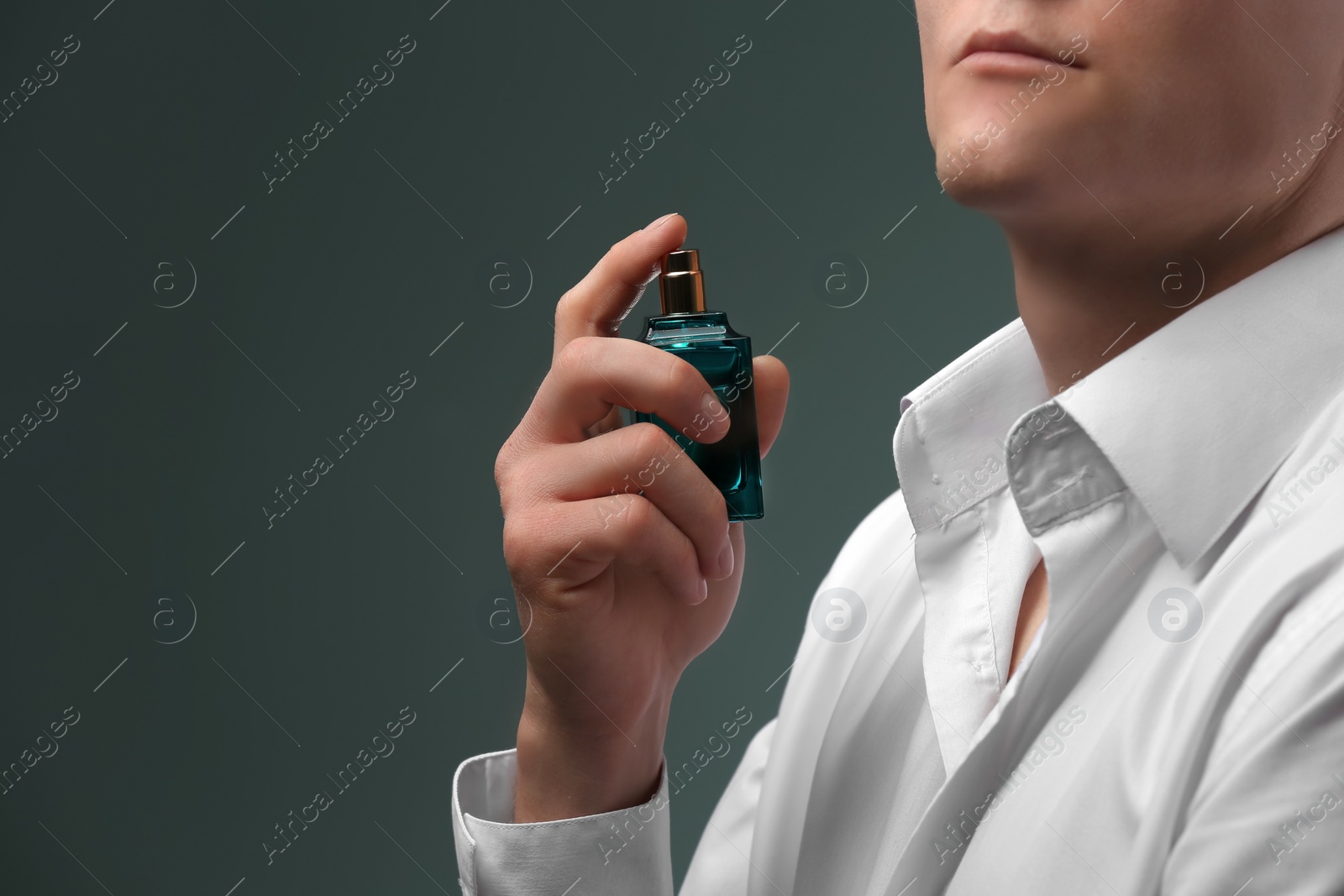 Photo of Handsome man in shirt using perfume on dark background, closeup