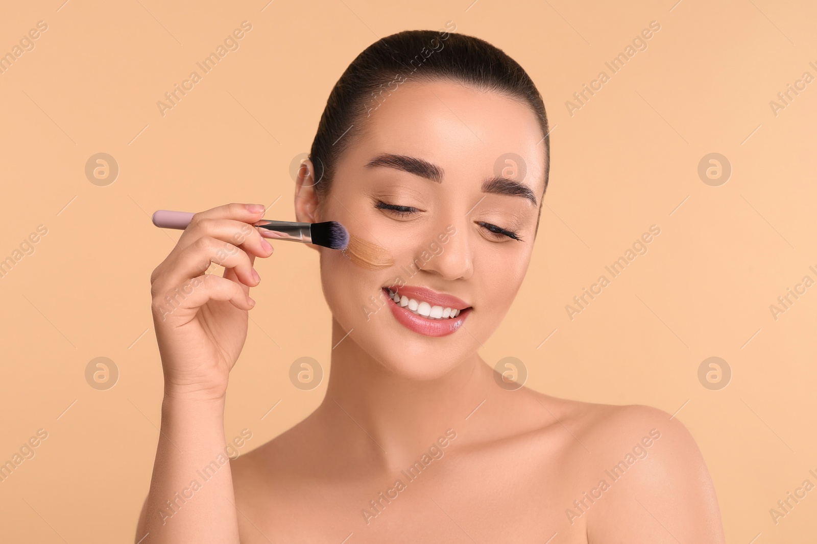 Photo of Woman applying foundation on face with brush against beige background