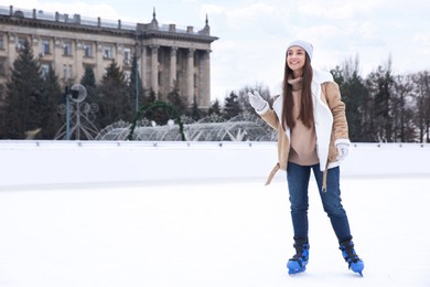 Happy woman skating along ice rink outdoors. Space for text