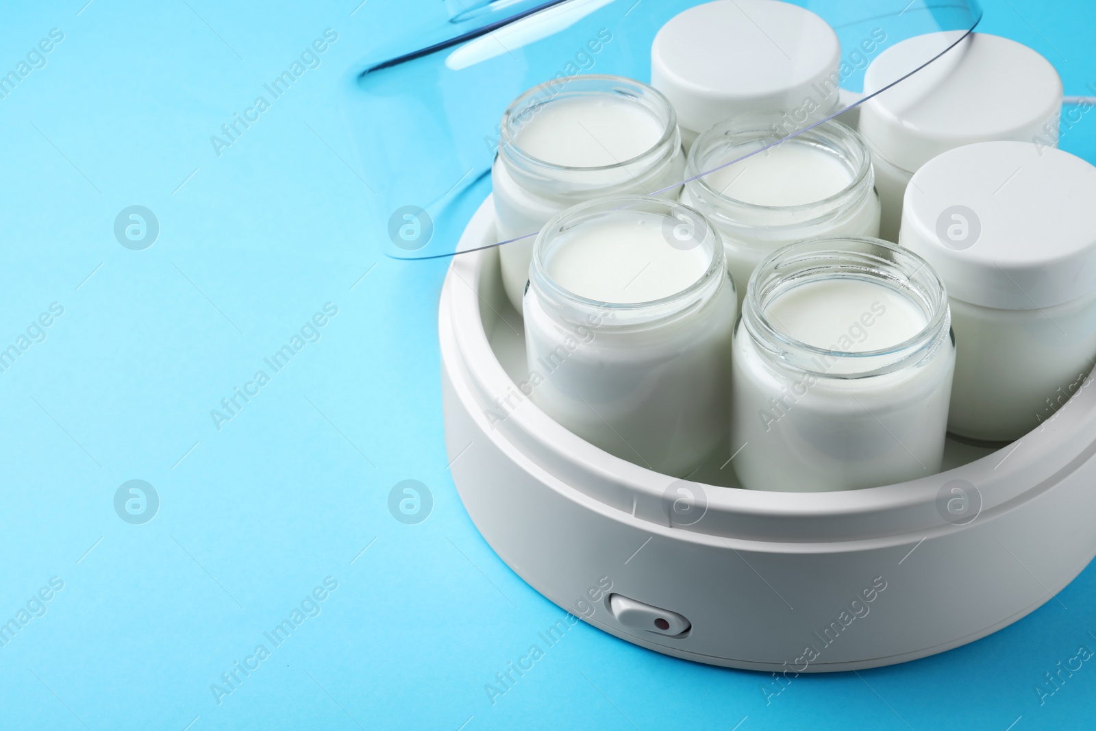 Photo of Modern yogurt maker with full jars on light blue background. Space for text