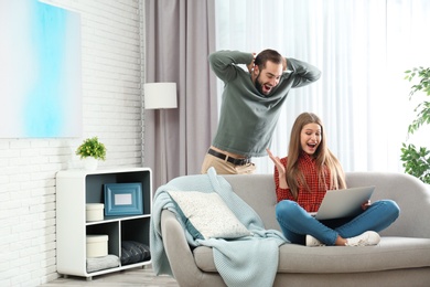 Photo of Emotional young couple with laptop celebrating victory at home