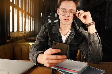 Photo of Teenage student using smartphone while studying at table in cafe