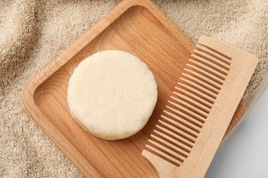 Photo of Solid shampoo bar, wooden comb and towel on light table, flat lay
