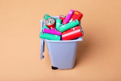 Photo of Many used batteries in recycling bin on light brown background