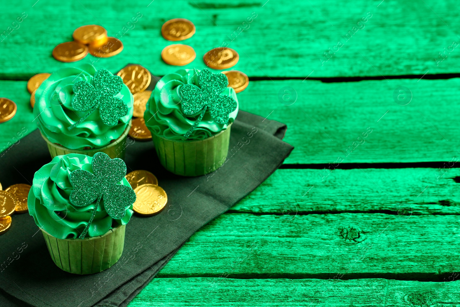 Image of St. Patrick's day. Tasty cupcakes with clover leaf toppers and cream on green wooden table, closeup. Space for text