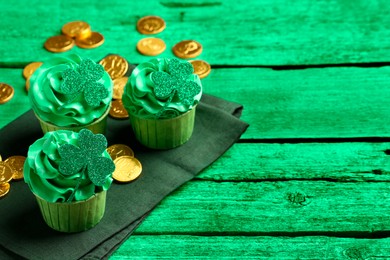 St. Patrick's day. Tasty cupcakes with clover leaf toppers and cream on green wooden table, closeup. Space for text