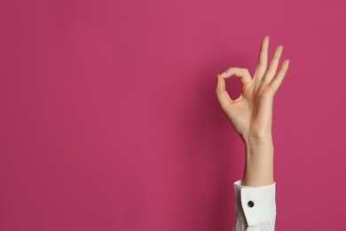 Young woman showing OK gesture on color background. Space for text