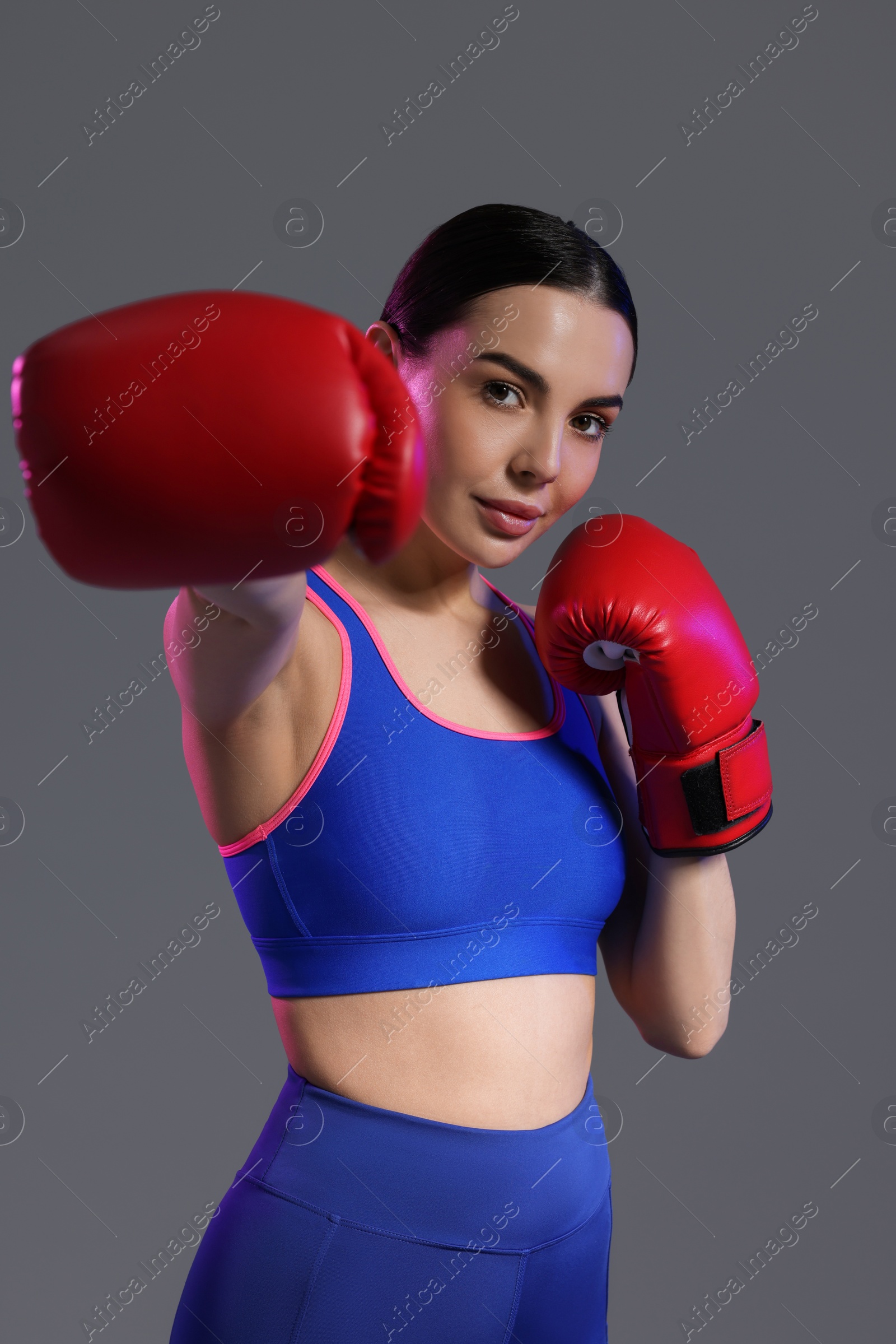 Photo of Portrait of beautiful woman wearing boxing gloves in color lights on grey background