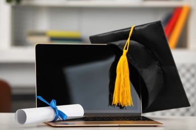 Photo of Graduation hat, student's diploma and laptop on white table indoors