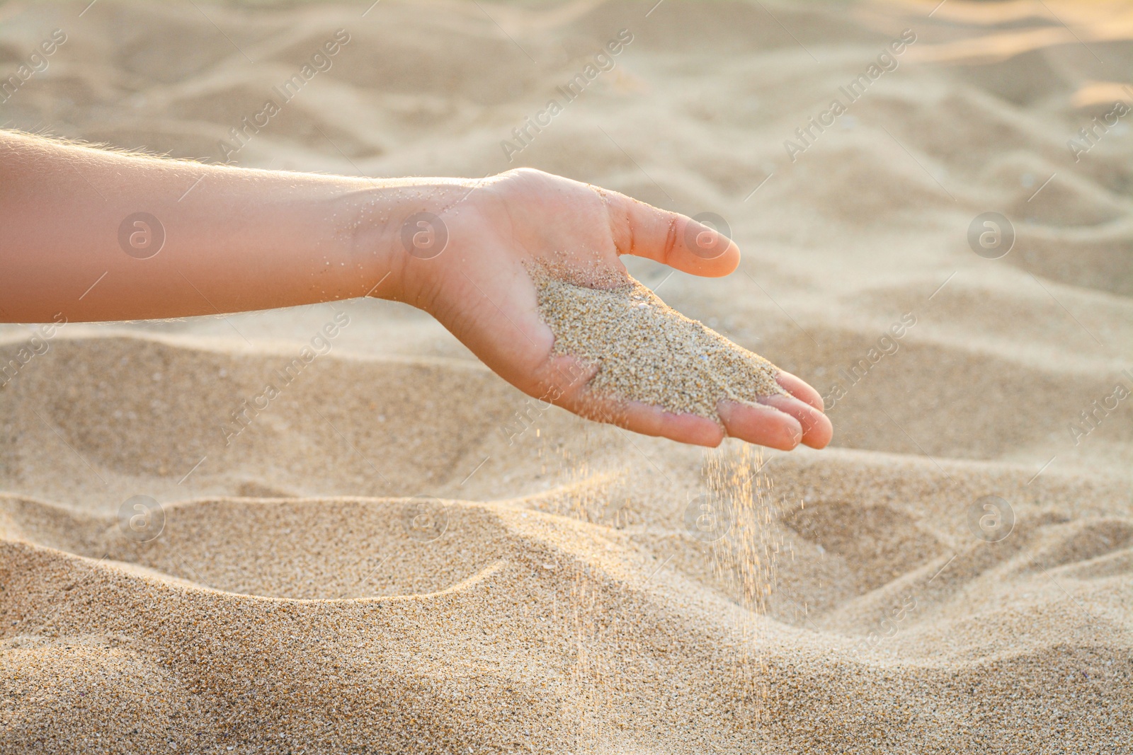 Photo of Girl pouring sand from hand outdoors, closeup. Fleeting time concept