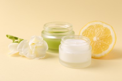 Moisturizing cream in open jars, lemon and freesia flower on beige background. Body care products