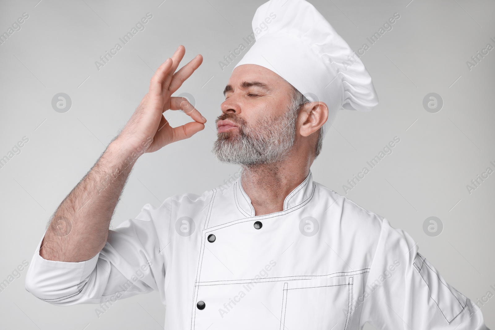 Photo of Chef in uniform showing perfect sign on grey background