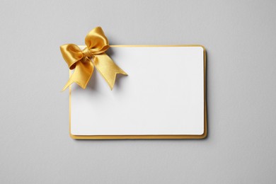 Photo of Blank gift card with golden bow on light grey background, top view. Space for text