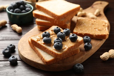 Photo of Delicious toasts with peanut butter and blueberries on wooden table, closeup