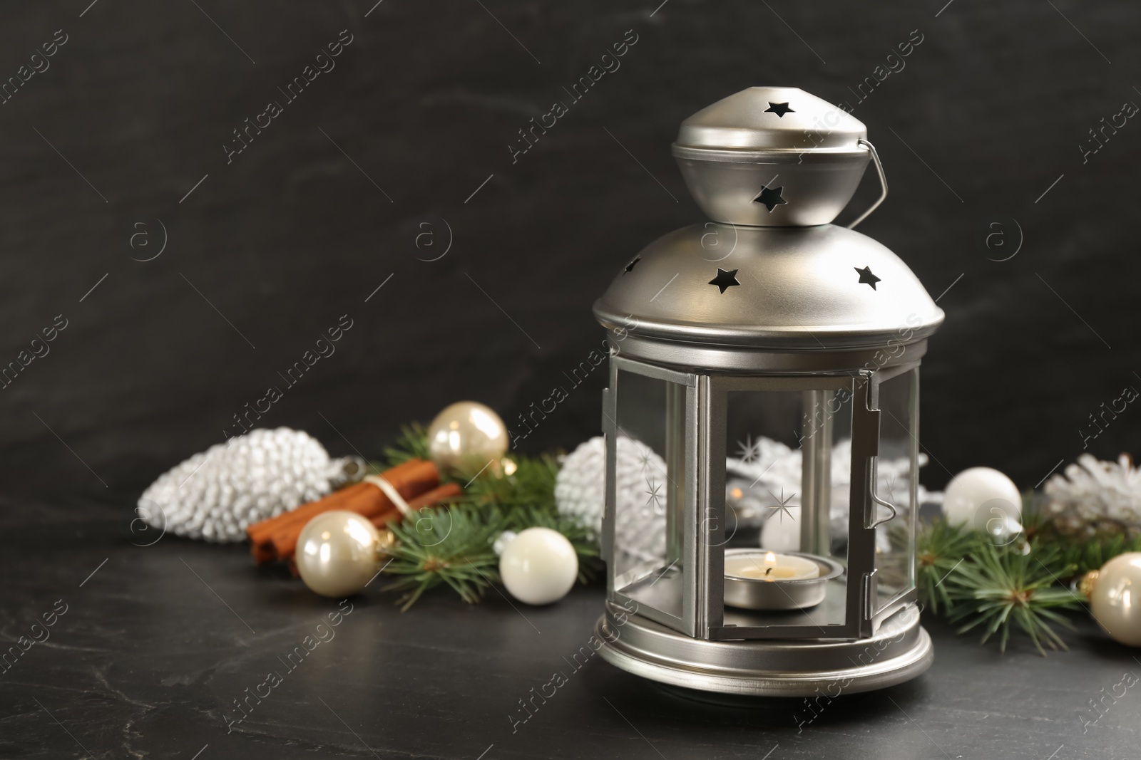 Photo of Christmas lantern with burning candle and festive decor on black table. Space for text