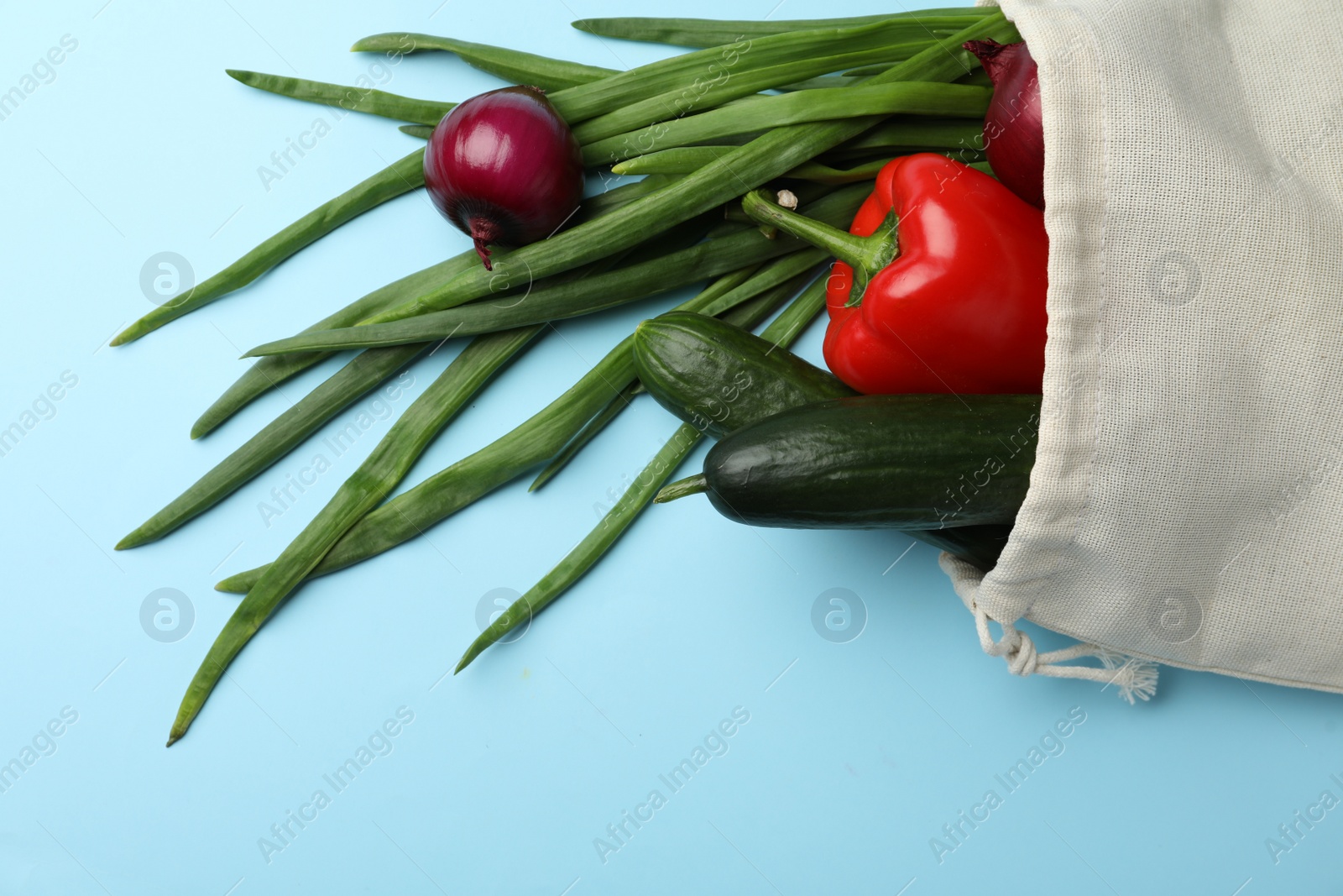 Photo of Cotton eco bag with vegetables on light blue background, top view