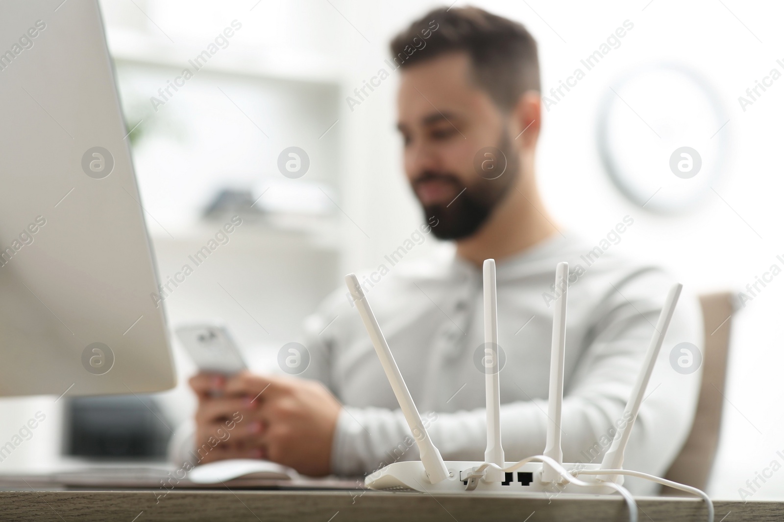 Photo of Man with smartphone working at wooden table indoors, focus on Wi-Fi router