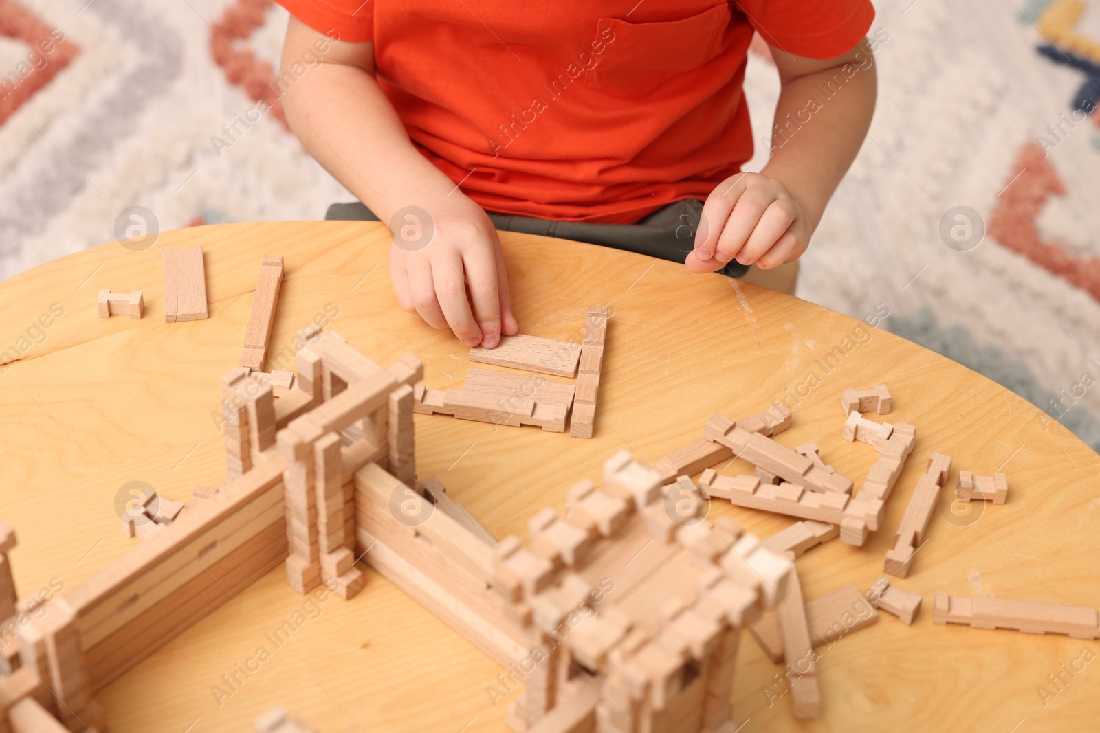 Photo of Little boy playing with wooden construction set at table in room, closeup. Child's toy