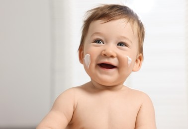 Photo of Cute little baby with moisturizing cream on face indoors