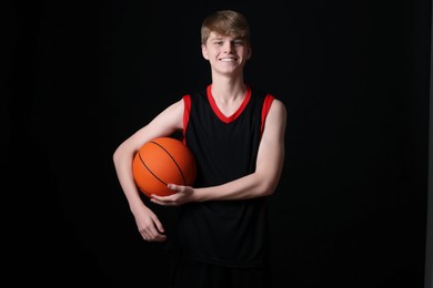 Teenage boy with basketball ball on black background