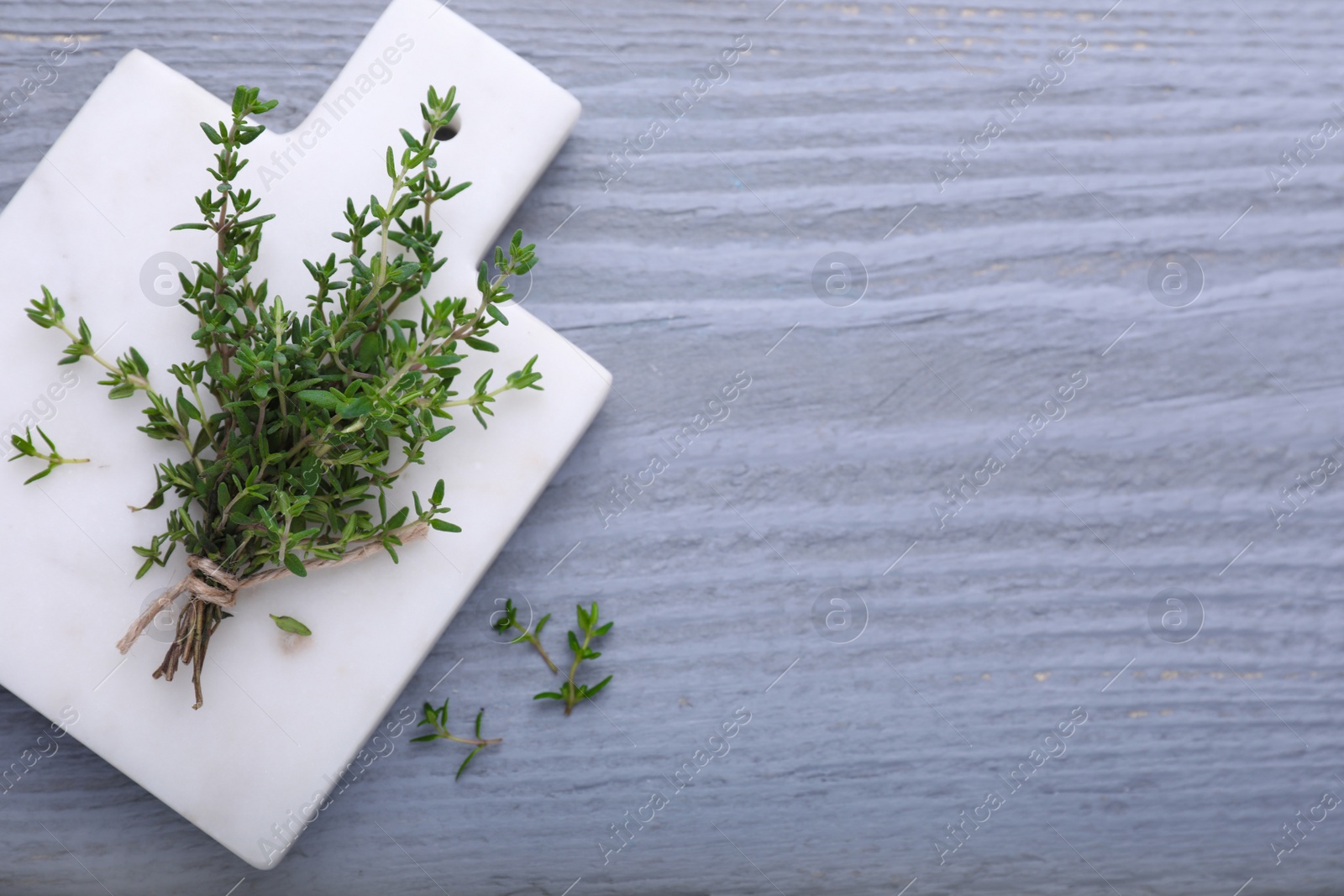 Photo of Board with aromatic fresh thyme on grey wooden table, top view. Space for text