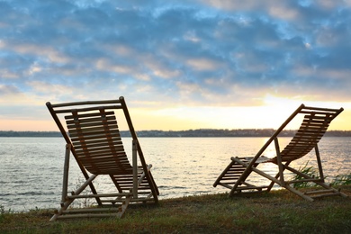 Photo of Empty wooden deckchairs on hill near calm river