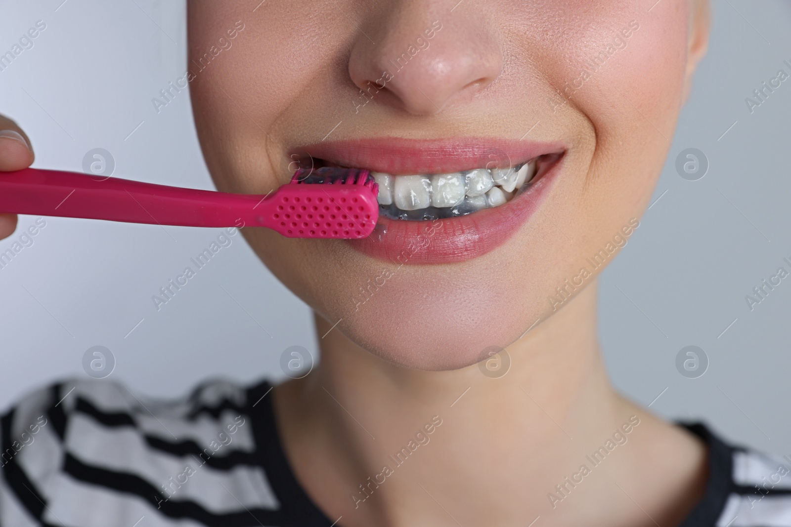 Photo of Woman brushing teeth with charcoal toothpaste on grey background, closeup