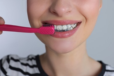 Photo of Woman brushing teeth with charcoal toothpaste on grey background, closeup